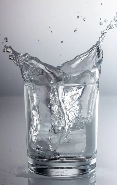 Wasser in ein Glas auf grauem Hintergrund sprühen — Stockfoto