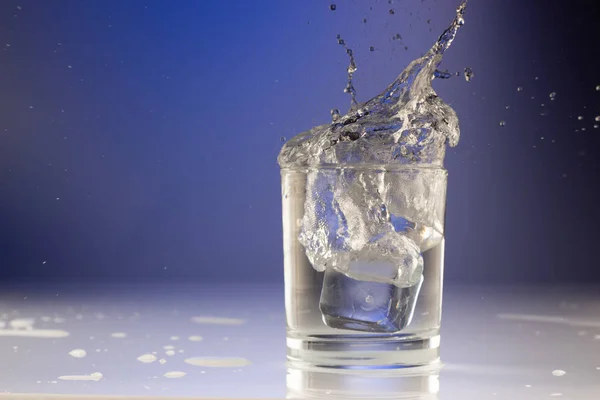 Wlewanie wody do szklanki na niebieskim tle z bliska — Zdjęcie stockowe
