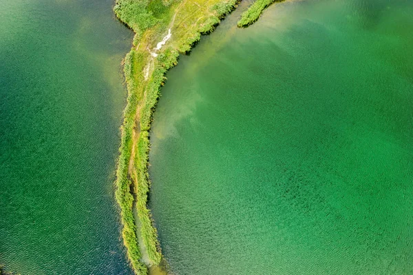 Una pequeña saliva con un camino cubierto de hierba verde a ambos lados, en un lago claro. Fotografía aérea — Foto de Stock