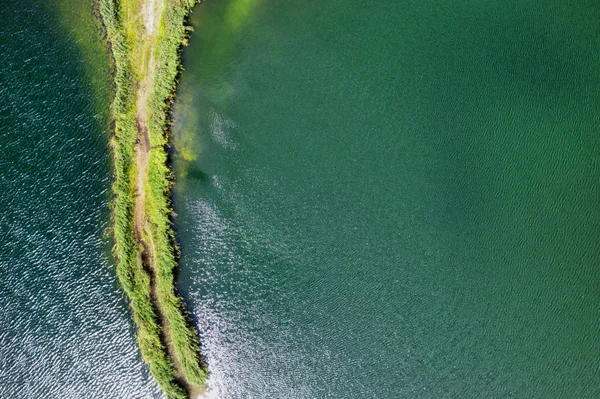 Una pequeña saliva con un camino cubierto de hierba verde a ambos lados, en un lago claro. Fotografía aérea — Foto de Stock
