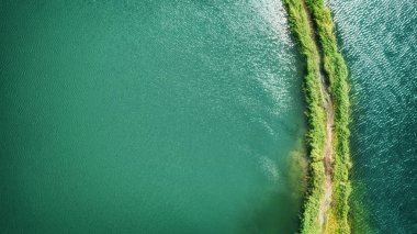 A small spit with a path covered with green grass on both sides, on a clear lake. Aerial photography clipart