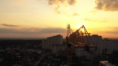 Endüstriyel inşaat vinçleri ve gün batımı arka plan ve gündoğumu üzerinde bina siluetleri.