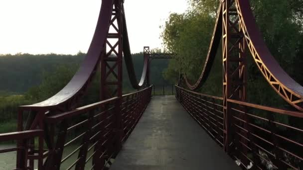De rode metalen brug over een kleine rivier op de dijk van de stad Irpin in Oekraïne, lage langzame drone vlucht — Stockvideo