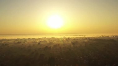 Sabah sisiyle kaplı köyün üzerinde şafağın 4K videosu. Güneş ışınları sisi güzelce kesti..