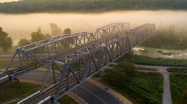 Sabah sisinde bir demiryolu köprüsü ya da güneş ışınlarının arka planda parladığı bir duman..