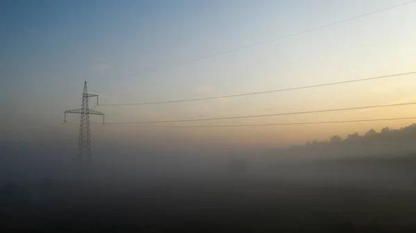 High voltage electricity transfer lines and pylon in a foggy morning
