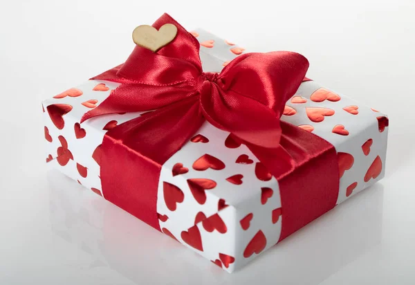 Ajándékdoboz, fehér papírba csomagolva, vörös szívstruktúrával. Rózsaszín szalagba csomagolva. — Stock Fotó