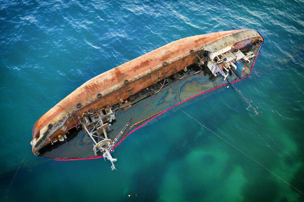 The tanker lies in the water on its side. Petroleum products leak and pollute the environment. Rusty sides of the tanker.
