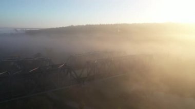 Şafakta, tren metal bir demiryolu köprüsünün üzerinden geçer. Bulanık nehir.