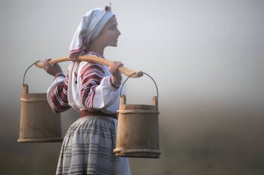 Genç ve çekici bir kadının omuzlarında nakışlı gömlek ve kovalar vardı..