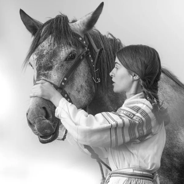 Young attractive woman in noble clothes stroking a horse.