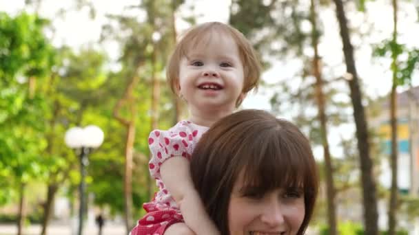 Feliz mamá lleva hermosa hijita en sus hombros, caminar en el parque con el niño — Vídeos de Stock