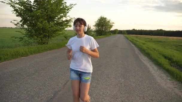 Beautiful girl doing sports exercises. girl in the music headphones runs along road. Slow motion — Stock Video