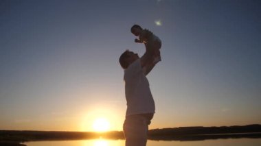 Babası küçük bebek kırmızı akşam güneşi kollarında tutar. Ağır çekim.