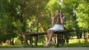 Gülümseyen ve yaz Park'ta dans mutlu genç kız banktaoturuyor, müzik dinlerken kulaklık.