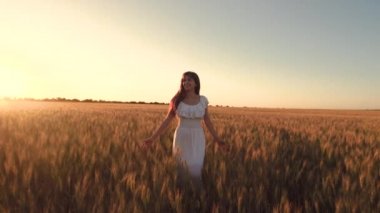 Mutlu kız uzun gelişmekte olan saç çalıştırmalar tarafından günbatımı kızdırma ve gülümsüyor altın buğday alanı ile. Ağır çekim