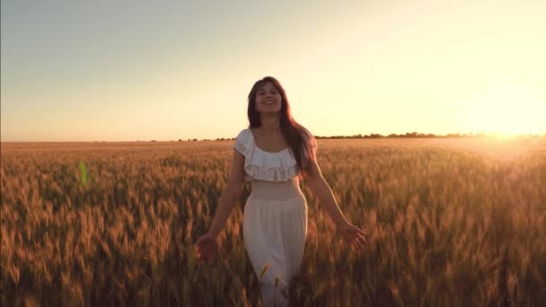 Смеющаяся девушка ходит по полю с пшеницей в сиянии золотого солнца. — стоковое видео