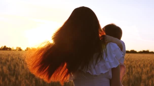 Mãe feliz com danças de criança pequenas e ri no brilho do pôr-do-sol de ouro em um campo de trigo. Movimento lento . — Vídeo de Stock