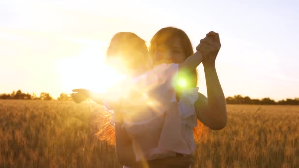 Junge Mutter mit kleinem Baby tanzt und lacht vor dem Hintergrund eines goldenen Sonnenuntergangs in einem Weizenfeld. Zeitlupe. — Stockvideo