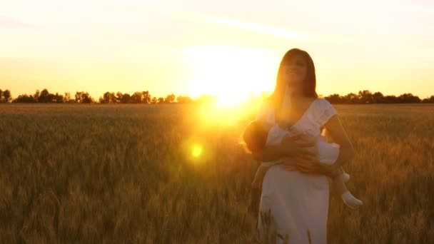 Pequeño niño en brazos de madre riendo en los rayos de la puesta de sol dorada en el campo de trigo. Movimiento lento . — Vídeos de Stock