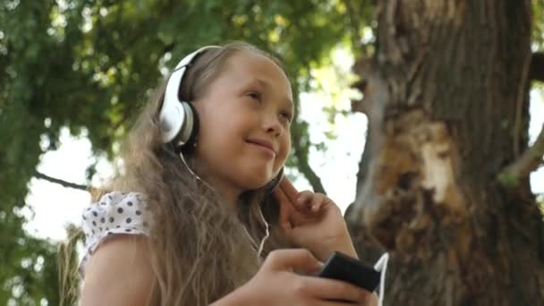 Счастливая девочка-подросток в наушниках слушает музыку и танцует в летнем парке — стоковое видео