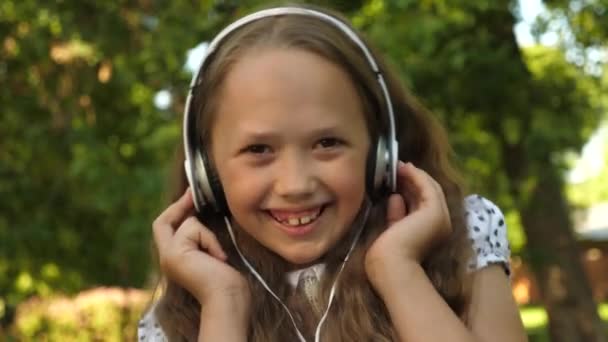 女孩在耳机听音乐和微笑跳舞在夏天公园 — 图库视频影像