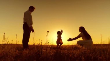 Anne çocuk ayaklarını altın günbatımı ışınları ile yürümeyi öğretmek.