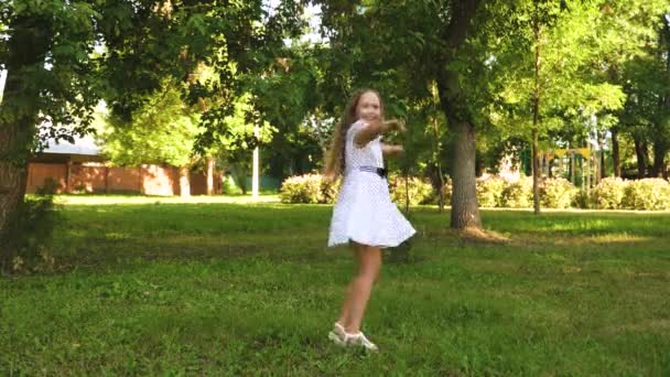 Adolescente chica está girando en un vestido de lunares blanco y sonriendo en un parque de verano . — Vídeos de Stock