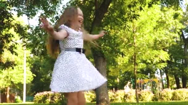 Teenage girl is spinning in a white polka dot dress and smiling in a summer park. — Stock Video