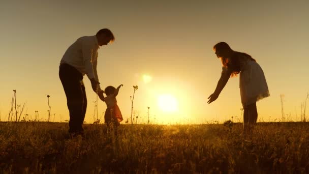 Young parents teach child to walk with their feet in rays of golden sunset.