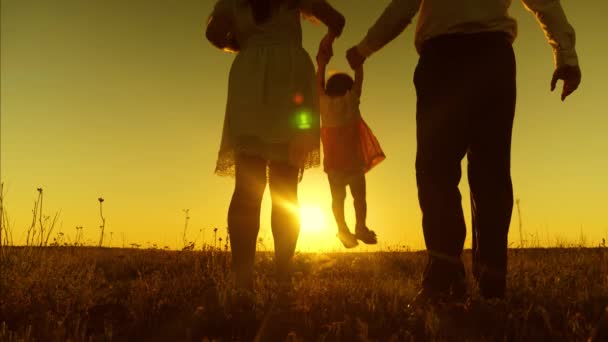 Bébé maman et papa marchent à travers le champ dans les rayons du soleil couchant et jouer avec l'enfant. Mouvement lent . — Video