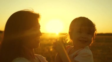 Mutlu çocuk gülünecek bir anne ellerinde altın güneş batımında oturan ellerini gürlemesi. Ağır çekim.