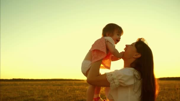 Mãe jovem e bonita com criança está brincando no ar no brilho do pôr do sol de ouro e rindo. Movimento lento . — Vídeo de Stock