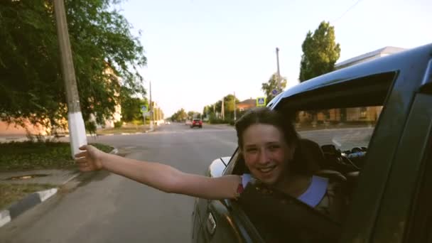 Mooi meisje rijdt een auto met haar handen uit het raam en lacht in het centrum van de stad. Slow motion. — Stockvideo