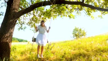 Yaz meşe beyaz elbise ve gülüyor altında salıncak üzerinde mutlu kız uzun saçlı hali.