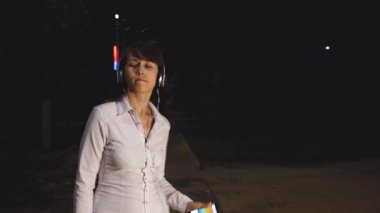 Kulaklık ile genç kız telefon dansları dokun ve gülümseyen ve bir adrenalin müzik geceleri şehir parkı içinde getting şarkı söylüyor
