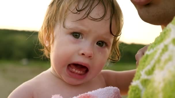 Litet barn fäller tårar och skrik när du sitter i handduk i händerna på pappa. Överordnade lugnar nyckfulla barn på stranden — Stockvideo
