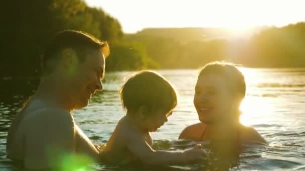 Младенец сестра и папа брызги и купание в воде, играя, улыбаясь и смеясь в золотом закате солнца — стоковое видео