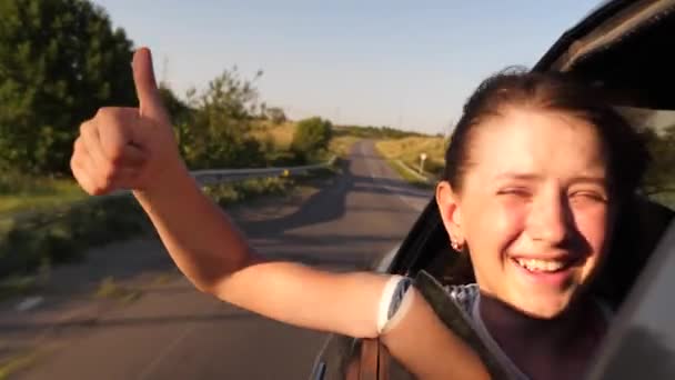 Dívka s dlouhými vlasy, sedící vpředu autě koukat z okna usmívat a ukazující ruka třída — Stock video