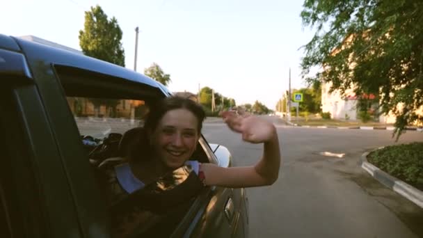 Hermosa chica con el pelo largo monta un coche con las manos por la ventana y sonriendo agitando su mano en el centro de la ciudad. Movimiento lento . — Vídeos de Stock