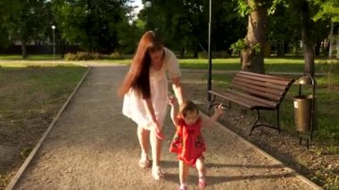 Anne küçük bebek yürüme ve Park yol boyunca yürüyüş gülümseyen öğrenir yakalar