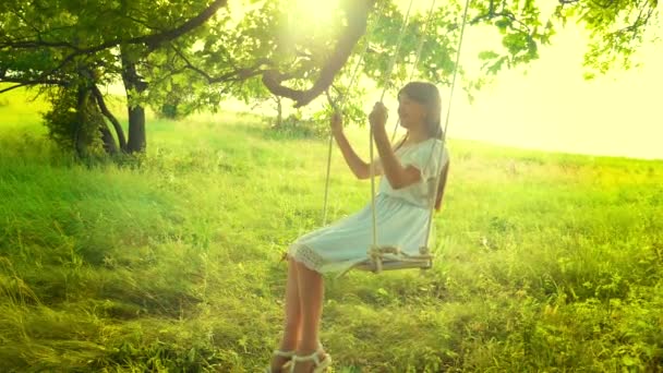 Young girl swings on a swing in the glare of a golden sunset and smiles. Slow motion. — Stock Video