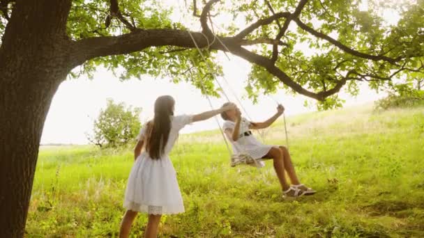 Las niñas con el pelo largo oscilación en balanceo y sonriendo felizmente bajo el roble de verano . — Vídeos de Stock