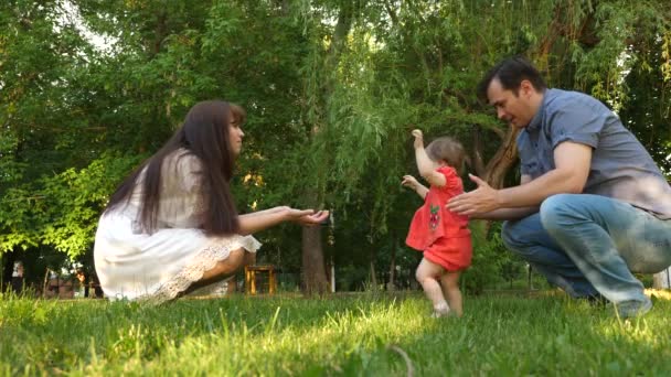 Barnet tar första stegen med hjälp av mamma och pappa på gräsmatta gräs. — Stockvideo