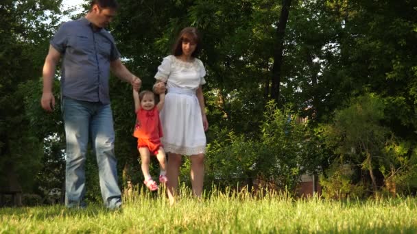 Baby mamma och pappa går runt hand i hand och spelar i stadsparken på gräsmatta gräs. Slow motion. — Stockvideo