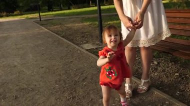Küçük bebek anne elini tutarak ve Park yol boyunca yürüyüş gülümseyen yürümeyi öğreniyor