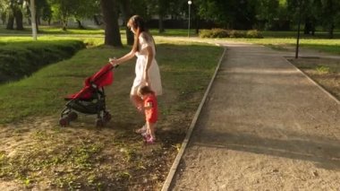 Küçük bebek kol tarafından park'ın annesiyle bebek arabası ile yürüyor