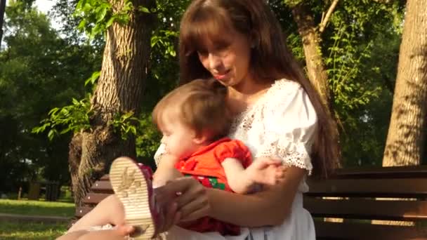 Moeder schoenen kind schoenen zitten op bankje in park zomer en lachend. Slow motion — Stockvideo