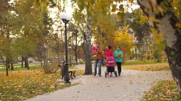 Glad mamma och pappa går med barn i höst park på väg under hösten skrattar och ler — Stockvideo