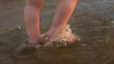 Küçük çocuk ilk adımları boyunca su tarafa sıçramasına nehir banka yapar. Bacaklar. Yakın çekim. Ağır çekim